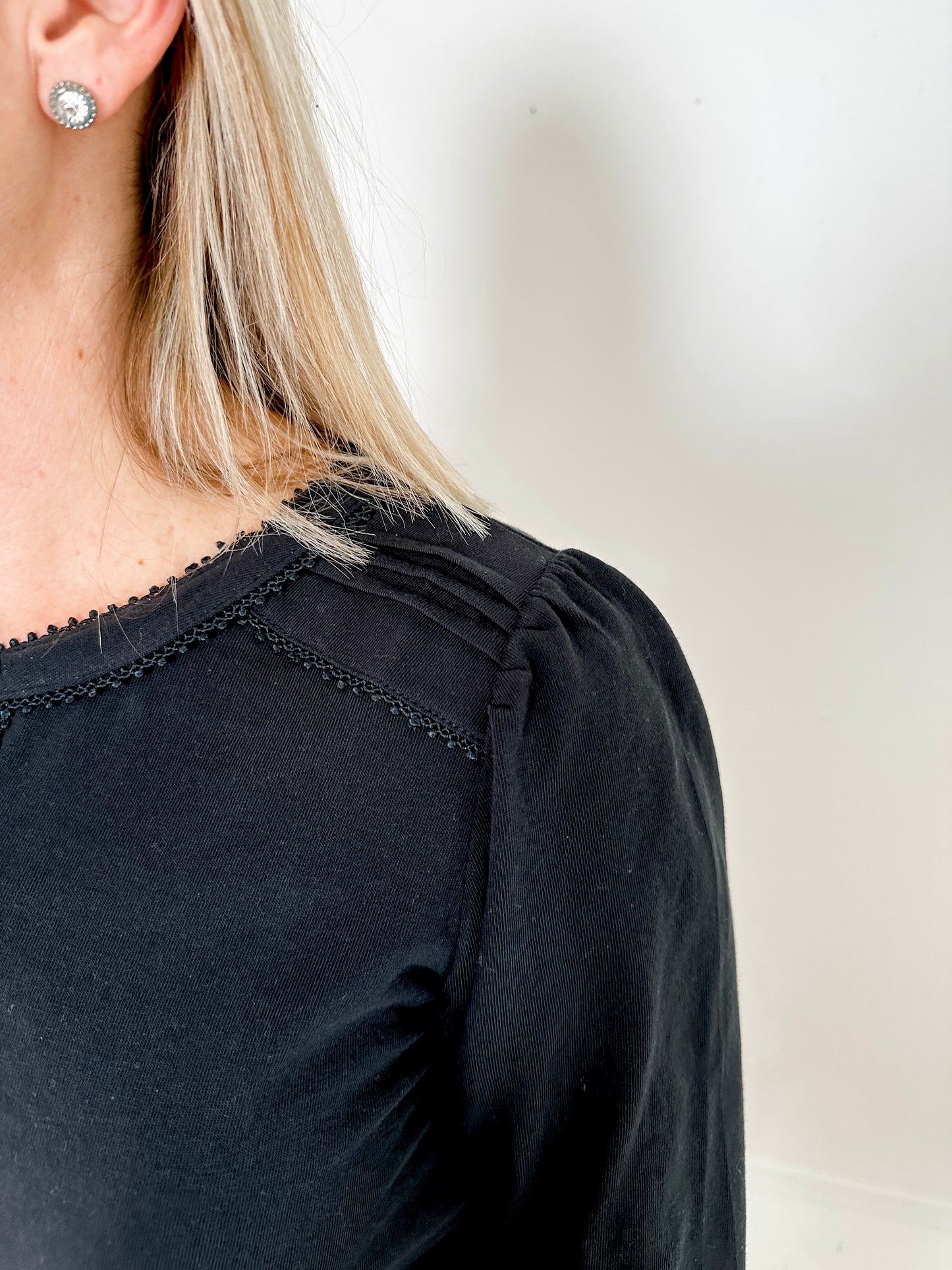 Women's knit blouse with lace detail, made from 100% cotton jersey surplus fabric. Available in black. Features a collarless band neckline, matching button-front placket, delicate knit lace on shoulders, collar, cuffs, and placket, keyhole buttoned cuffs, and side slits. Medium-weight fabric with light stretch for a straight fit. Available in sizes XS-3X.