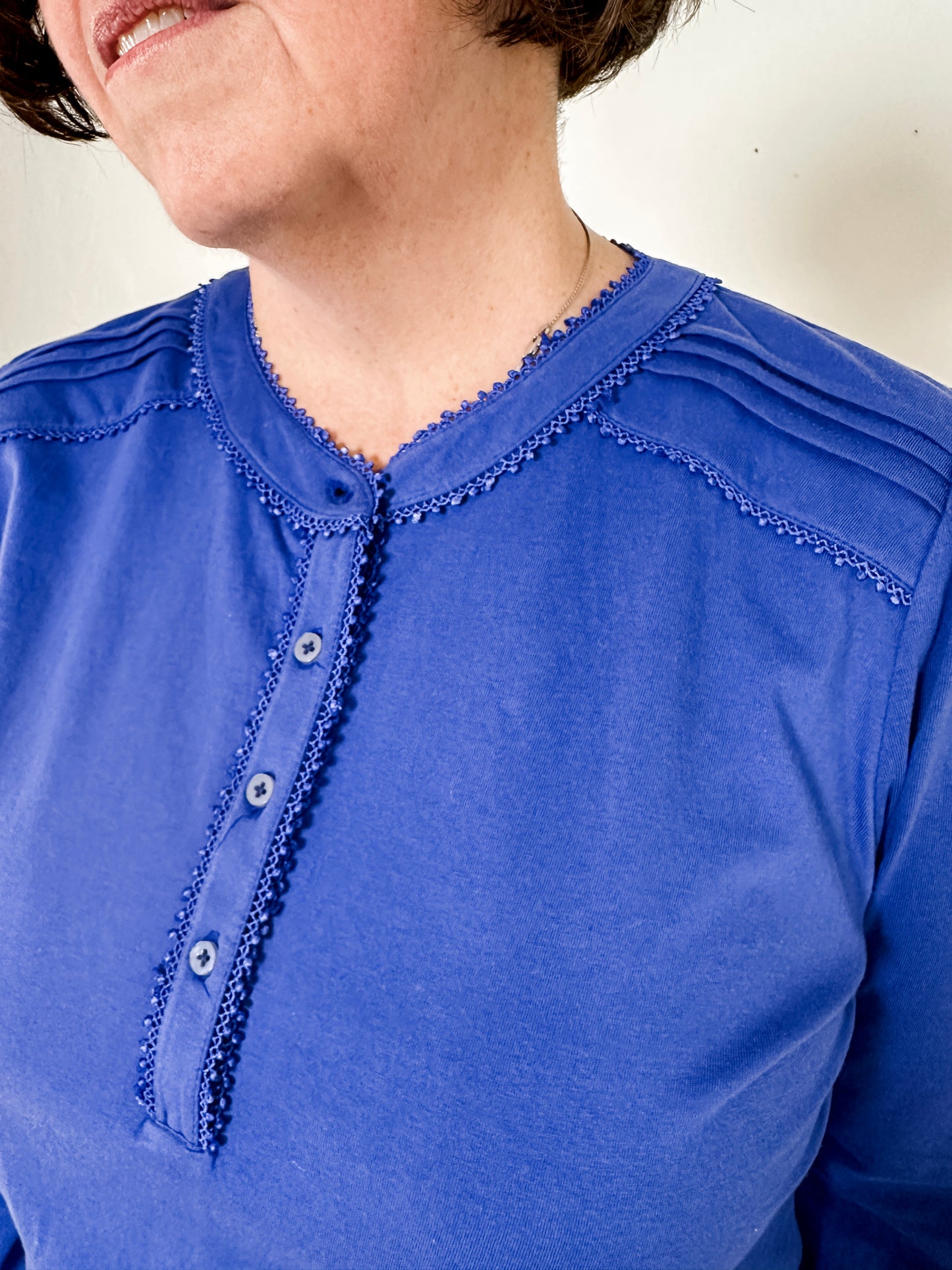 Women's knit blouse with lace detail, made from 100% cotton jersey surplus fabric. Available in sapphire. Features a collarless band neckline, matching button-front placket, delicate knit lace on shoulders, collar, cuffs, and placket, keyhole buttoned cuffs, and side slits. Medium-weight fabric with light stretch for a straight fit. Available in sizes XS-3X.