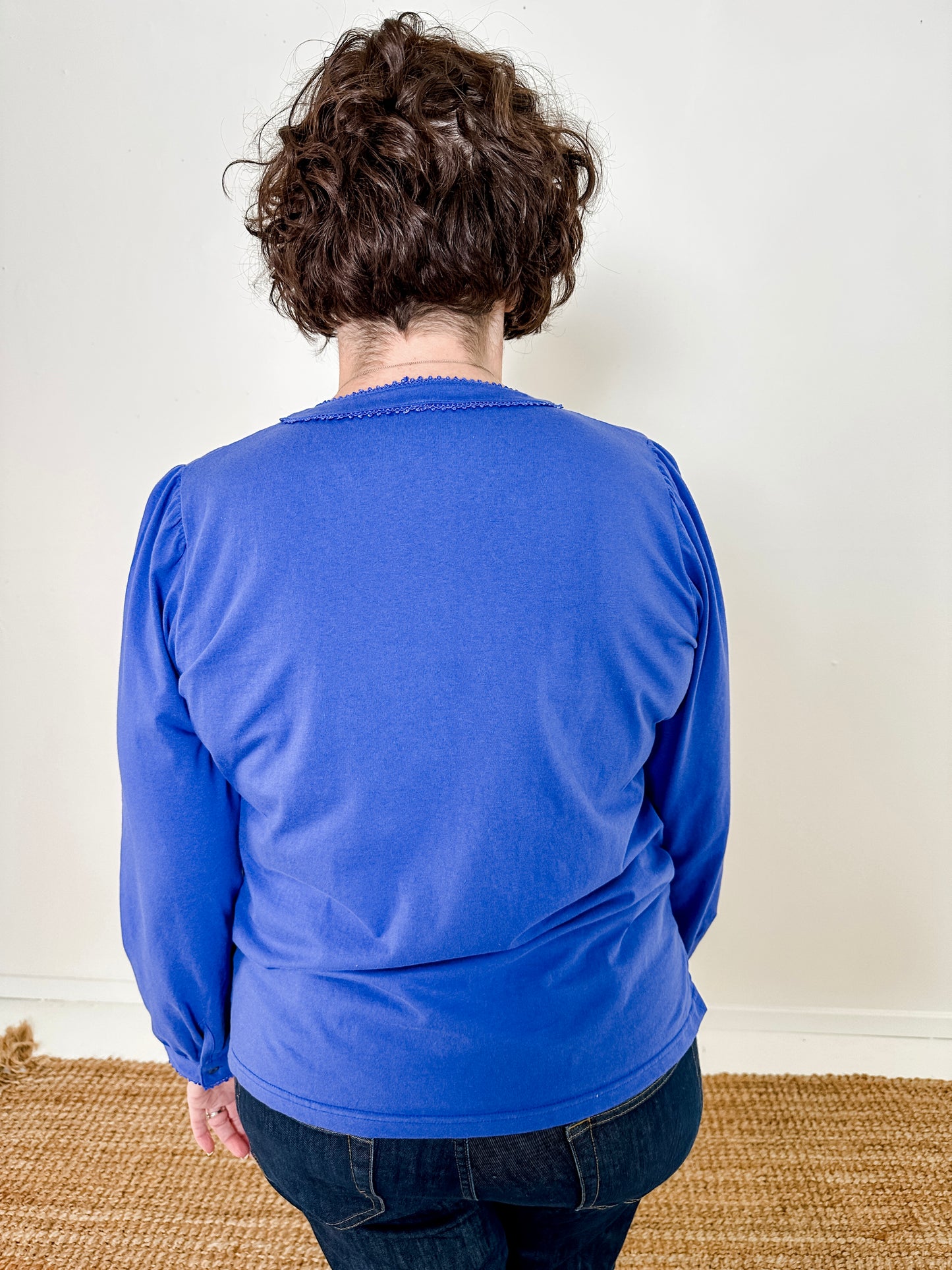Women's knit blouse with lace detail, made from 100% cotton jersey surplus fabric. Available in sapphire. Features a collarless band neckline, matching button-front placket, delicate knit lace on shoulders, collar, cuffs, and placket, keyhole buttoned cuffs, and side slits. Medium-weight fabric with light stretch for a straight fit. Available in sizes XS-3X.