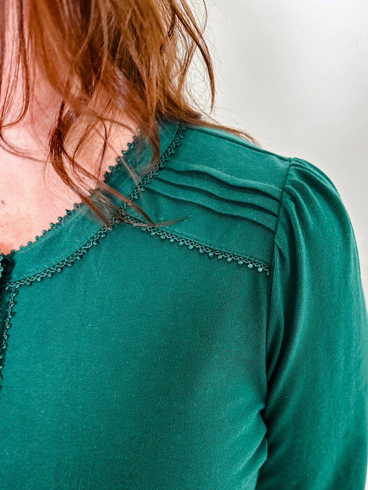 Women's knit blouse with lace detail, made from 100% cotton jersey surplus fabric. Available in Evergreen. Features a collarless band neckline, matching button-front placket, delicate knit lace on shoulders, collar, cuffs, and placket, keyhole buttoned cuffs, and side slits. Medium-weight fabric with light stretch for a straight fit. Available in sizes XS-3X.