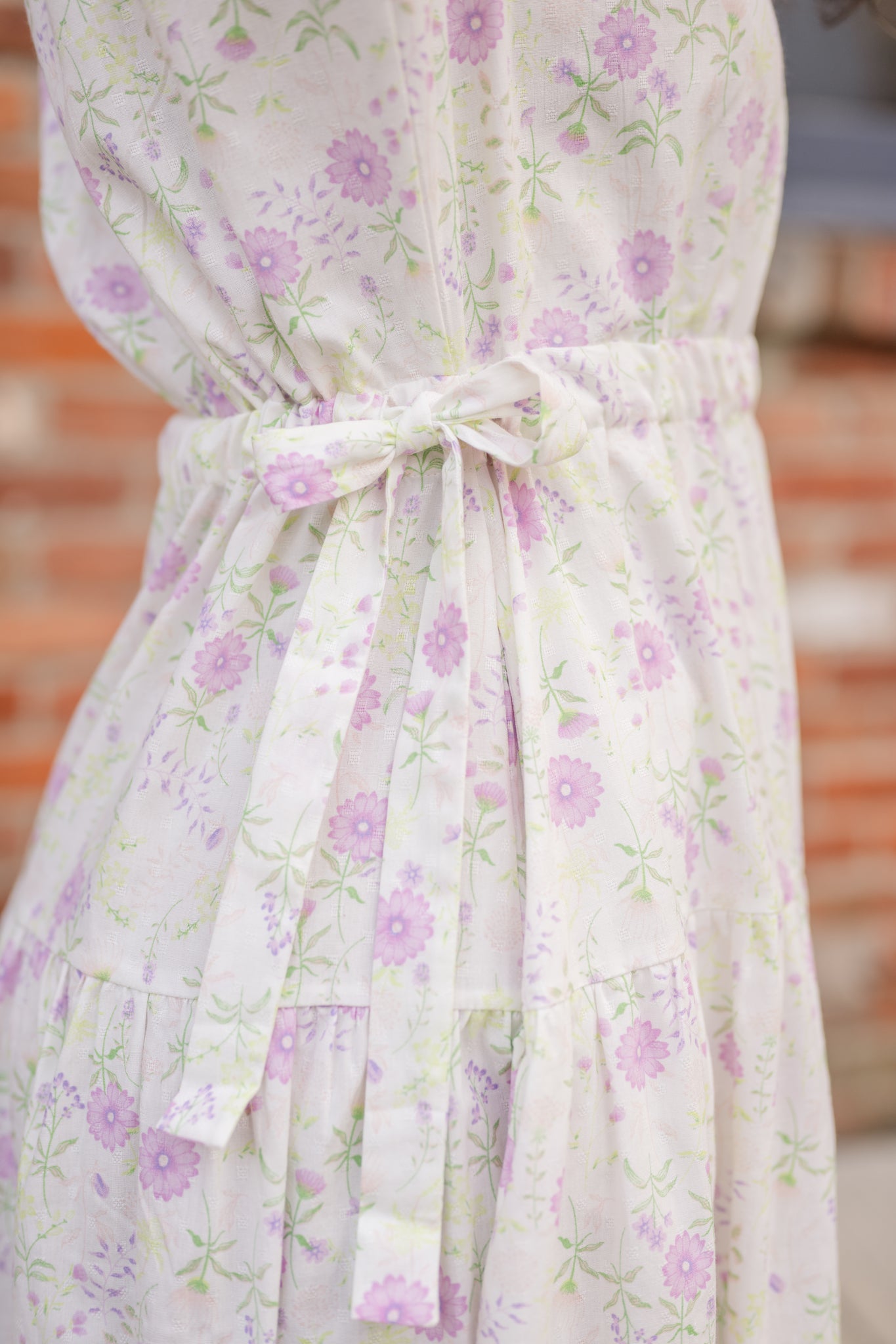 Elegant midi-length dress in surplus 100% cotton with puff sleeves and a unique V-neckline. Features ruching along the bodice, shoulders, and skirt, plus drawstring bows at the waist for a flattering fit. Designed with hidden side pockets, elbow-length keyhole cuff sleeves, and a box-pleated hem. Finished with French seams and a hidden decorative placket.