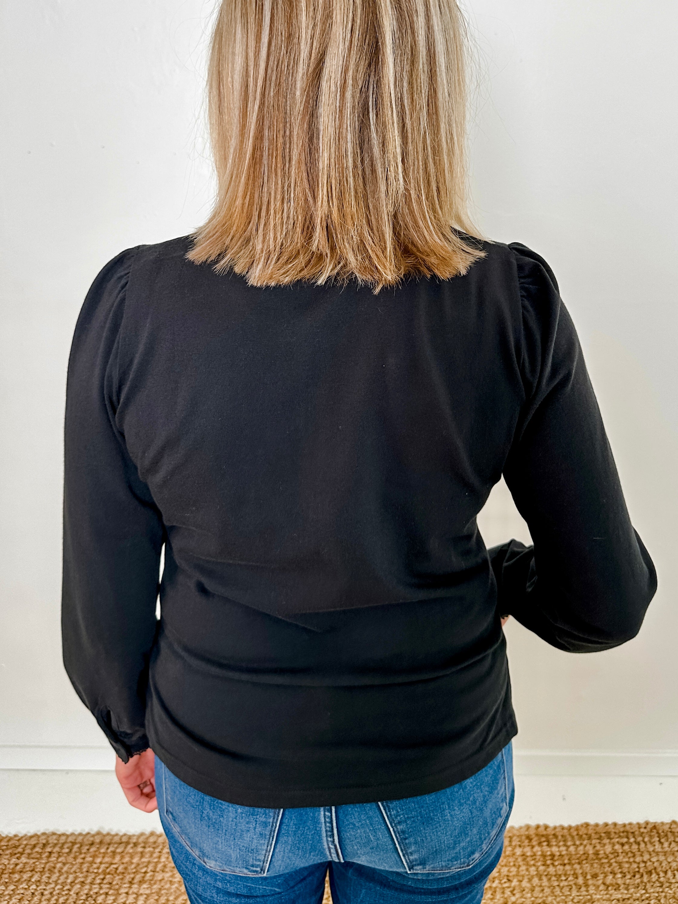 Women's knit blouse with lace detail, made from 100% cotton jersey surplus fabric. Available in black. Features a collarless band neckline, matching button-front placket, delicate knit lace on shoulders, collar, cuffs, and placket, keyhole buttoned cuffs, and side slits. Medium-weight fabric with light stretch for a straight fit. Available in sizes XS-3X.