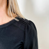 Women's knit blouse with lace detail, made from 100% cotton jersey surplus fabric. Available in black. Features a collarless band neckline, matching button-front placket, delicate knit lace on shoulders, collar, cuffs, and placket, keyhole buttoned cuffs, and side slits. Medium-weight fabric with light stretch for a straight fit. Available in sizes XS-3X.