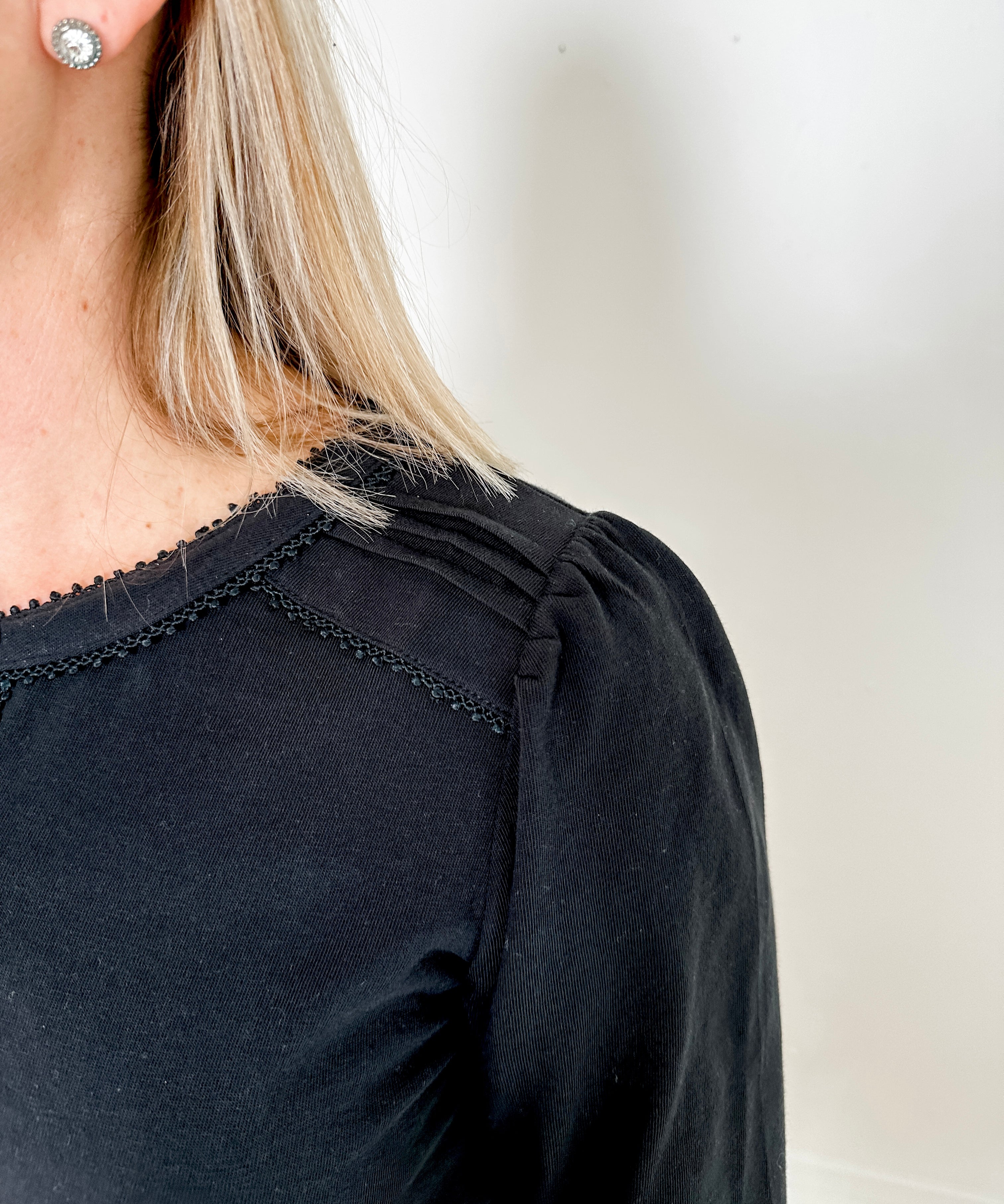 Women's knit blouse with lace detail, made from 100% cotton jersey surplus fabric. Available in black. Features a collarless band neckline, matching button-front placket, delicate knit lace on shoulders, collar, cuffs, and placket, keyhole buttoned cuffs, and side slits. Medium-weight fabric with light stretch for a straight fit. Available in sizes XS-3X.