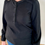 Women's knit blouse with lace detail, made from 100% cotton jersey surplus fabric. Available in black. Features a collarless band neckline, matching button-front placket, delicate knit lace on shoulders, collar, cuffs, and placket, keyhole buttoned cuffs, and side slits. Medium-weight fabric with light stretch for a straight fit. Available in sizes XS-3X.