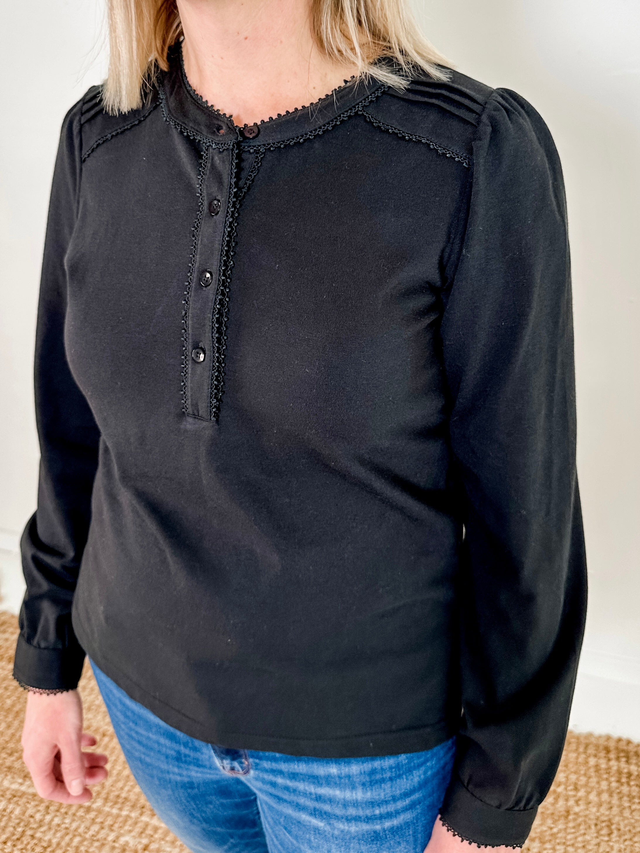 Women's knit blouse with lace detail, made from 100% cotton jersey surplus fabric. Available in black. Features a collarless band neckline, matching button-front placket, delicate knit lace on shoulders, collar, cuffs, and placket, keyhole buttoned cuffs, and side slits. Medium-weight fabric with light stretch for a straight fit. Available in sizes XS-3X.