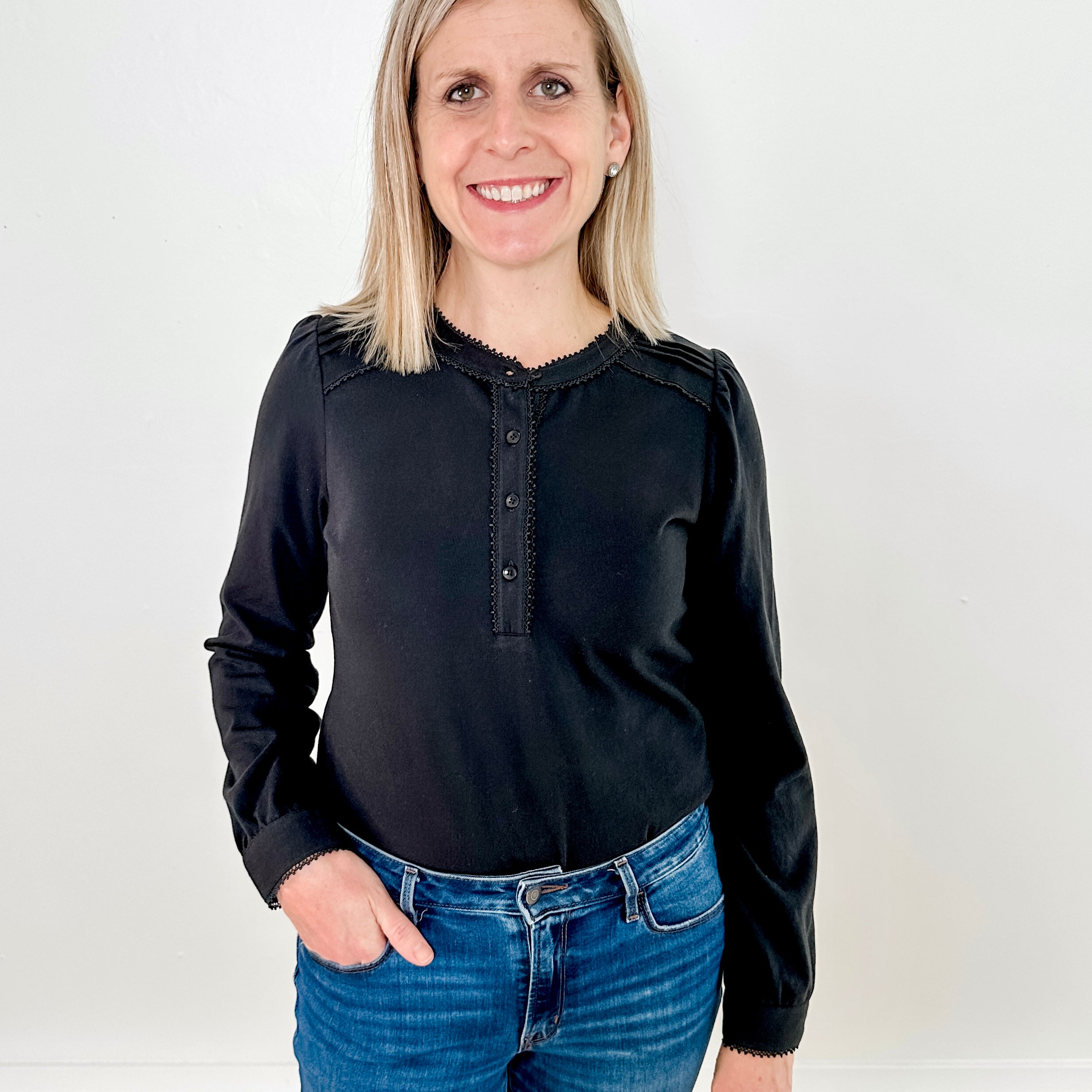 Women's knit blouse with lace detail, made from 100% cotton jersey surplus fabric. Available in black. Features a collarless band neckline, matching button-front placket, delicate knit lace on shoulders, collar, cuffs, and placket, keyhole buttoned cuffs, and side slits. Medium-weight fabric with light stretch for a straight fit. Available in sizes XS-3X.