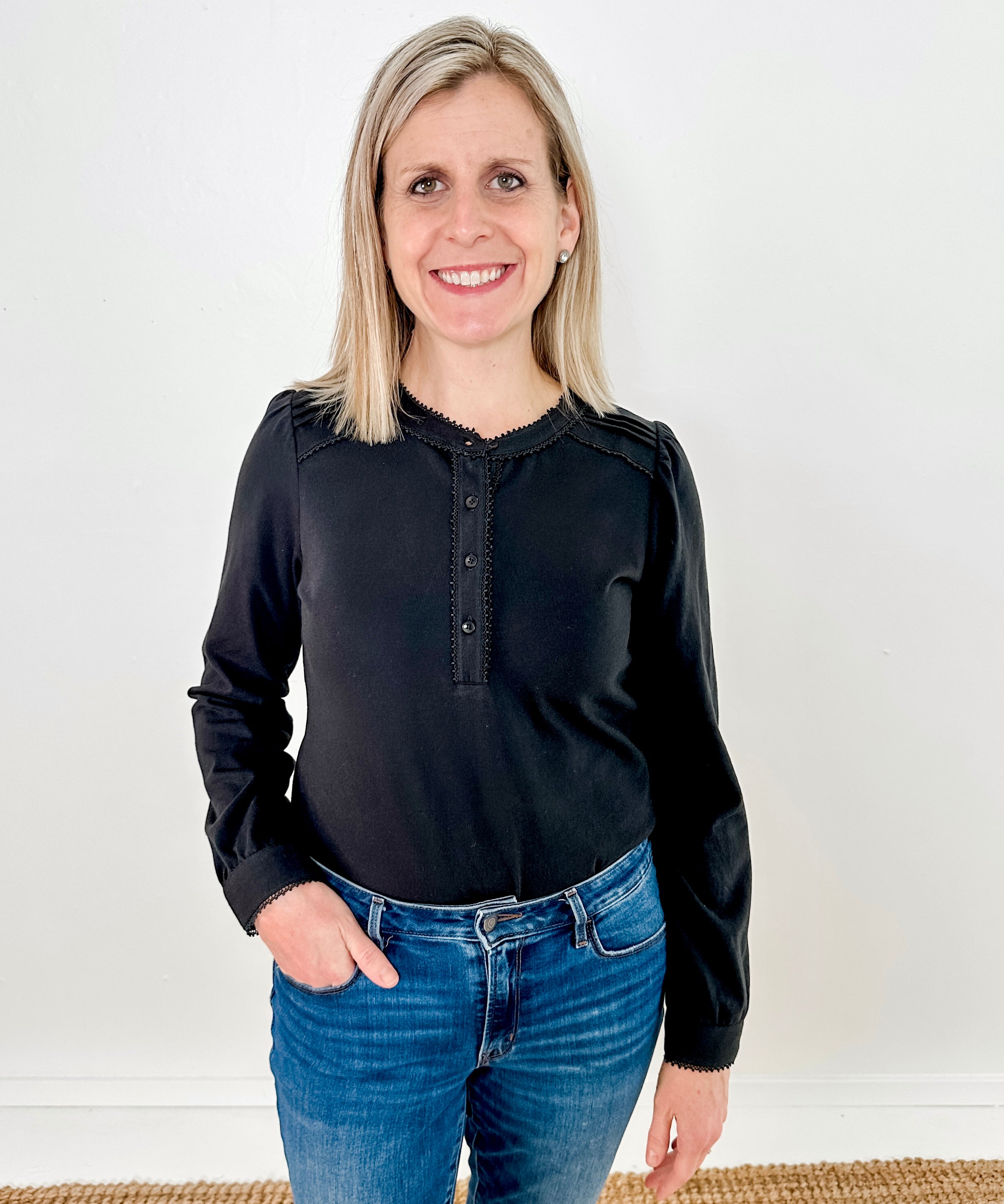 Women's knit blouse with lace detail, made from 100% cotton jersey surplus fabric. Available in black. Features a collarless band neckline, matching button-front placket, delicate knit lace on shoulders, collar, cuffs, and placket, keyhole buttoned cuffs, and side slits. Medium-weight fabric with light stretch for a straight fit. Available in sizes XS-3X.