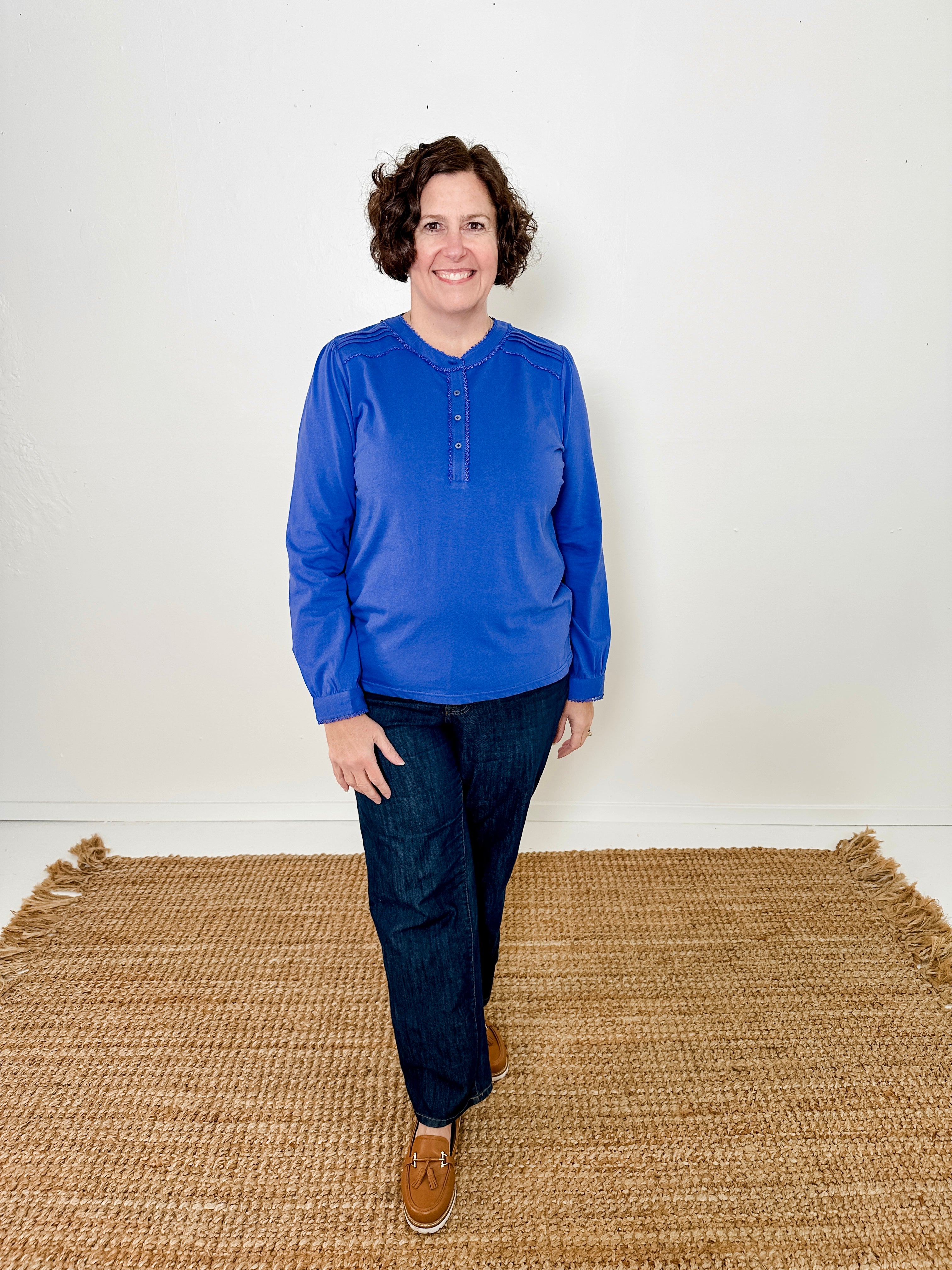 Women's knit blouse with lace detail, made from 100% cotton jersey surplus fabric. Available in sapphire. Features a collarless band neckline, matching button-front placket, delicate knit lace on shoulders, collar, cuffs, and placket, keyhole buttoned cuffs, and side slits. Medium-weight fabric with light stretch for a straight fit. Available in sizes XS-3X.