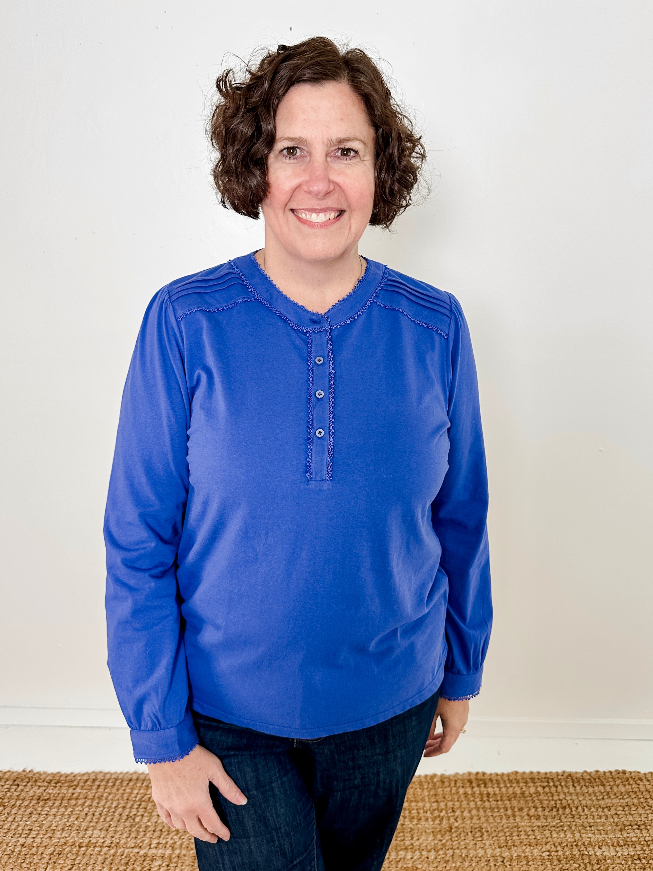 Women's knit blouse with lace detail, made from 100% cotton jersey surplus fabric. Available in sapphire. Features a collarless band neckline, matching button-front placket, delicate knit lace on shoulders, collar, cuffs, and placket, keyhole buttoned cuffs, and side slits. Medium-weight fabric with light stretch for a straight fit. Available in sizes XS-3X.