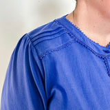 Women's knit blouse with lace detail, made from 100% cotton jersey surplus fabric. Available in sapphire. Features a collarless band neckline, matching button-front placket, delicate knit lace on shoulders, collar, cuffs, and placket, keyhole buttoned cuffs, and side slits. Medium-weight fabric with light stretch for a straight fit. Available in sizes XS-3X.