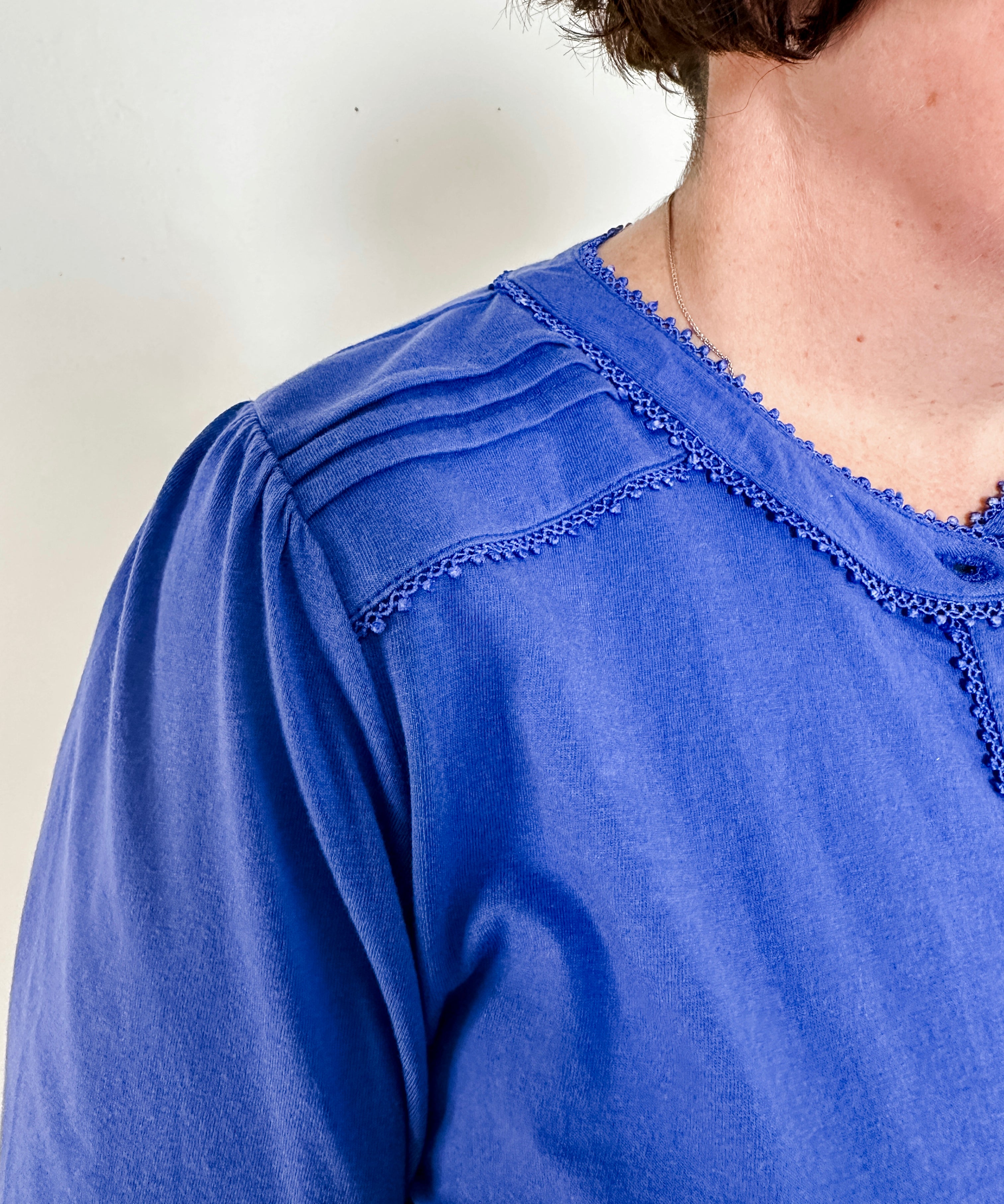 Women's knit blouse with lace detail, made from 100% cotton jersey surplus fabric. Available in sapphire. Features a collarless band neckline, matching button-front placket, delicate knit lace on shoulders, collar, cuffs, and placket, keyhole buttoned cuffs, and side slits. Medium-weight fabric with light stretch for a straight fit. Available in sizes XS-3X.