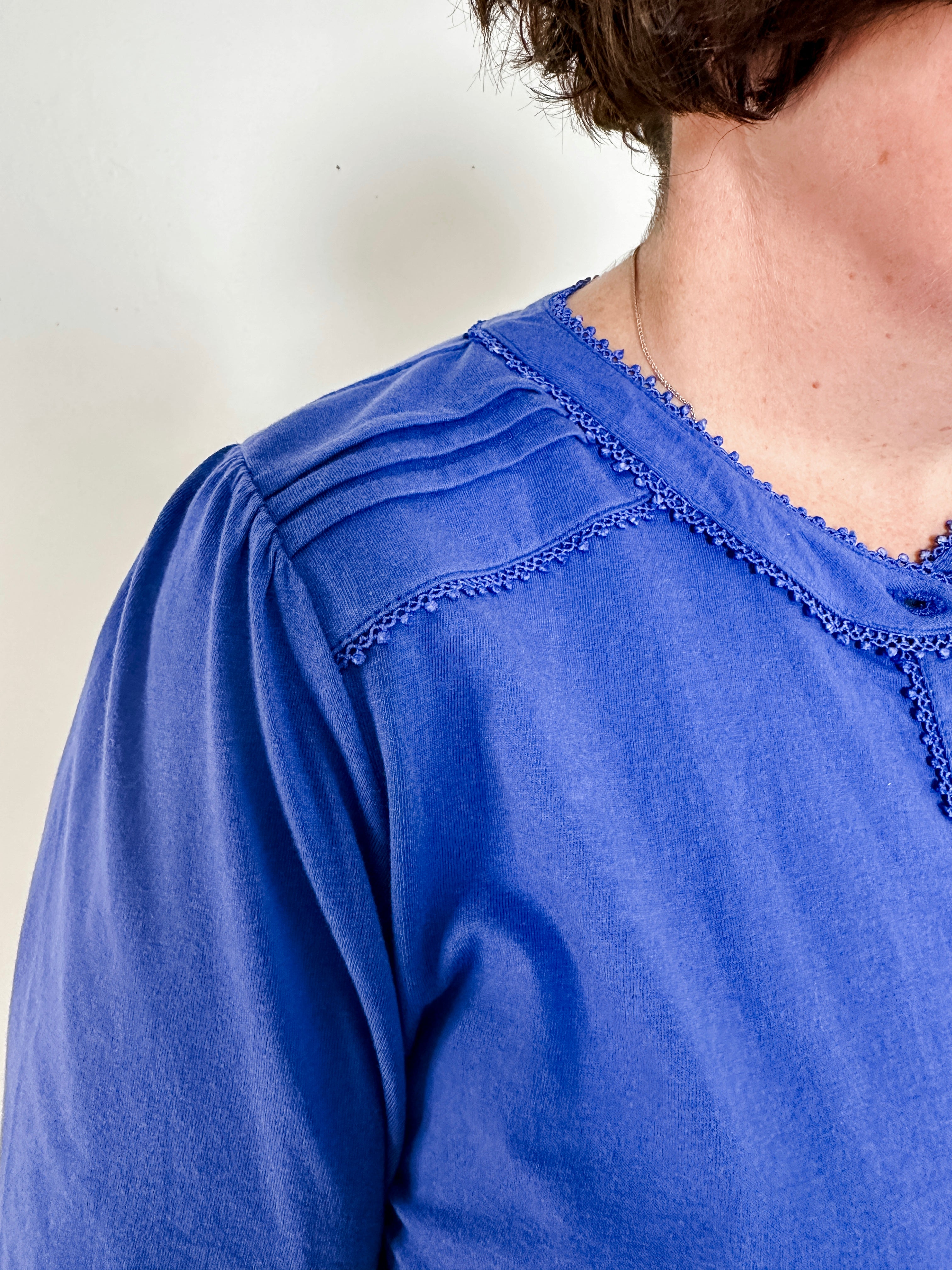Women's knit blouse with lace detail, made from 100% cotton jersey surplus fabric. Available in sapphire. Features a collarless band neckline, matching button-front placket, delicate knit lace on shoulders, collar, cuffs, and placket, keyhole buttoned cuffs, and side slits. Medium-weight fabric with light stretch for a straight fit. Available in sizes XS-3X.
