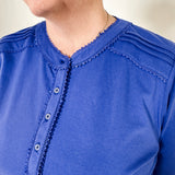 Women's knit blouse with lace detail, made from 100% cotton jersey surplus fabric. Available in sapphire. Features a collarless band neckline, matching button-front placket, delicate knit lace on shoulders, collar, cuffs, and placket, keyhole buttoned cuffs, and side slits. Medium-weight fabric with light stretch for a straight fit. Available in sizes XS-3X.