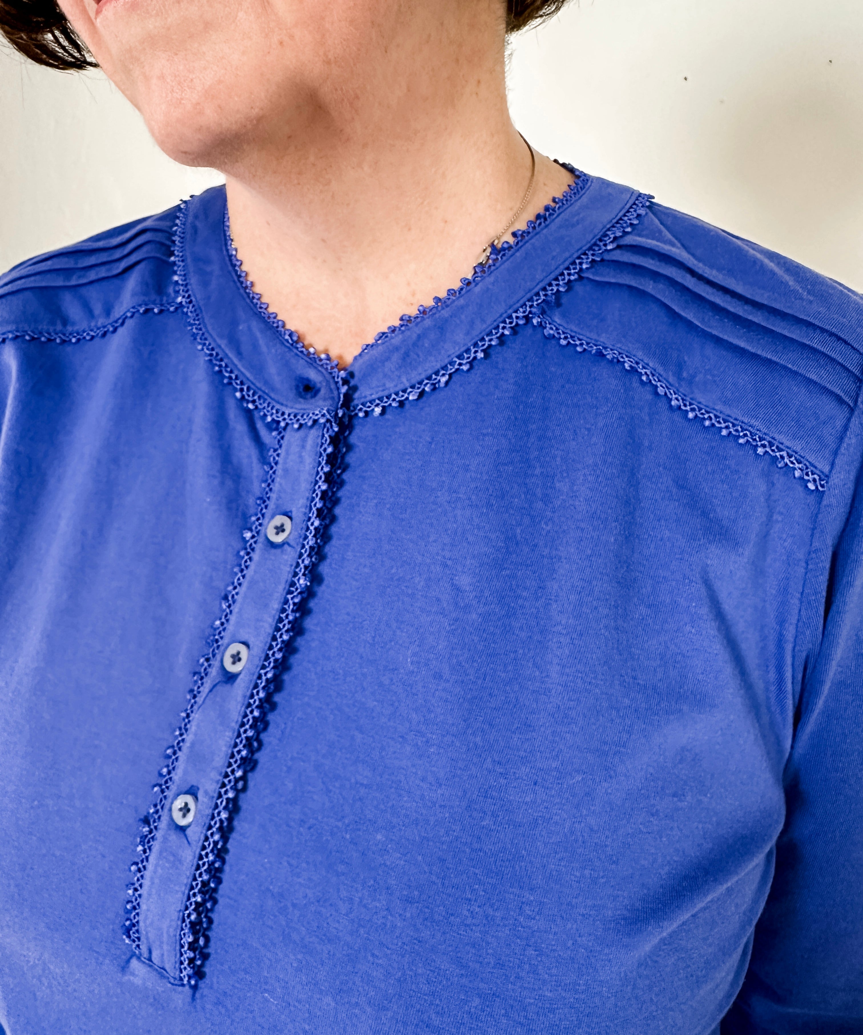 Women's knit blouse with lace detail, made from 100% cotton jersey surplus fabric. Available in sapphire. Features a collarless band neckline, matching button-front placket, delicate knit lace on shoulders, collar, cuffs, and placket, keyhole buttoned cuffs, and side slits. Medium-weight fabric with light stretch for a straight fit. Available in sizes XS-3X.