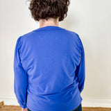 Women's knit blouse with lace detail, made from 100% cotton jersey surplus fabric. Available in sapphire. Features a collarless band neckline, matching button-front placket, delicate knit lace on shoulders, collar, cuffs, and placket, keyhole buttoned cuffs, and side slits. Medium-weight fabric with light stretch for a straight fit. Available in sizes XS-3X.