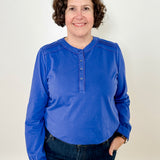 Women's knit blouse with lace detail, made from 100% cotton jersey surplus fabric. Available in sapphire. Features a collarless band neckline, matching button-front placket, delicate knit lace on shoulders, collar, cuffs, and placket, keyhole buttoned cuffs, and side slits. Medium-weight fabric with light stretch for a straight fit. Available in sizes XS-3X.