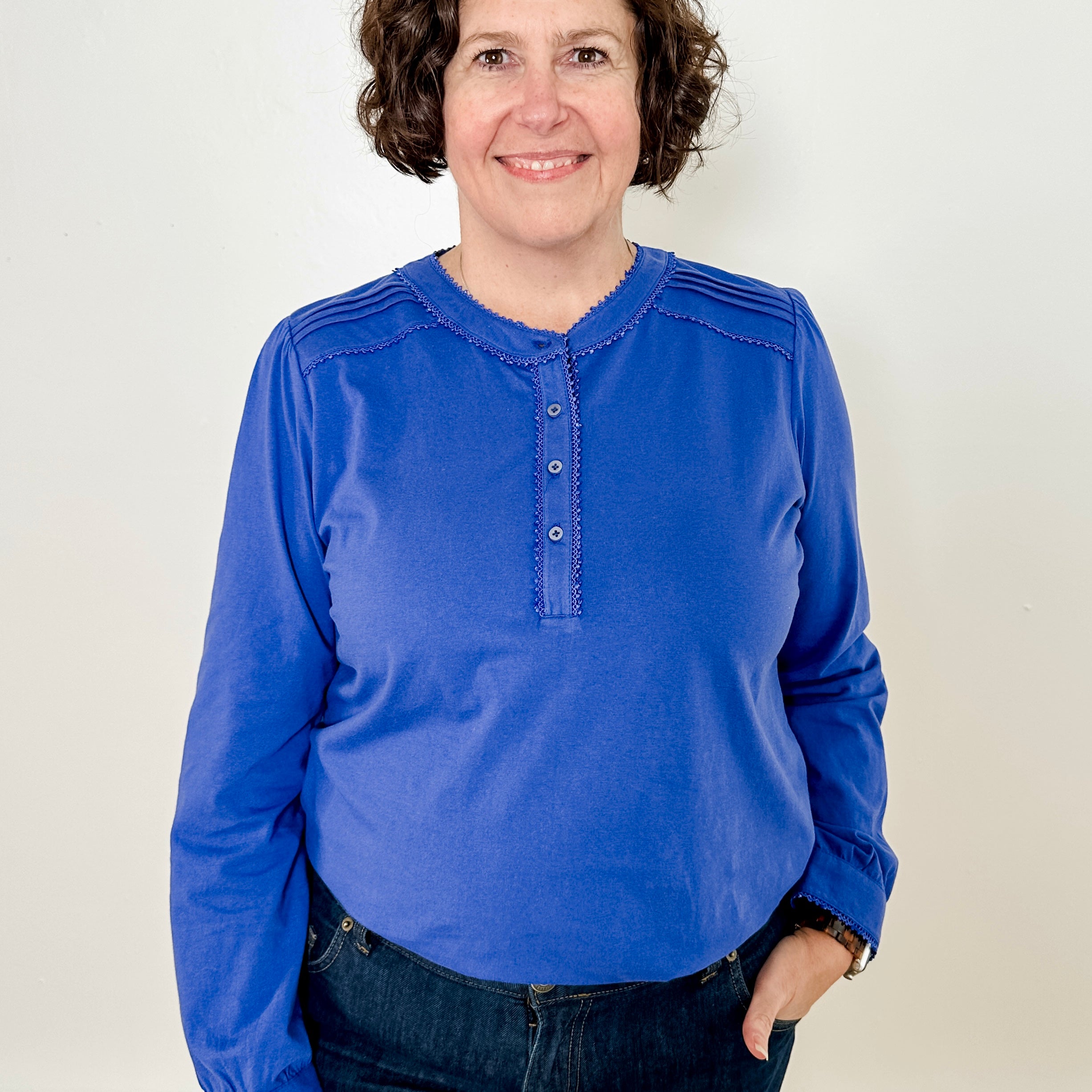 Women's knit blouse with lace detail, made from 100% cotton jersey surplus fabric. Available in sapphire. Features a collarless band neckline, matching button-front placket, delicate knit lace on shoulders, collar, cuffs, and placket, keyhole buttoned cuffs, and side slits. Medium-weight fabric with light stretch for a straight fit. Available in sizes XS-3X.