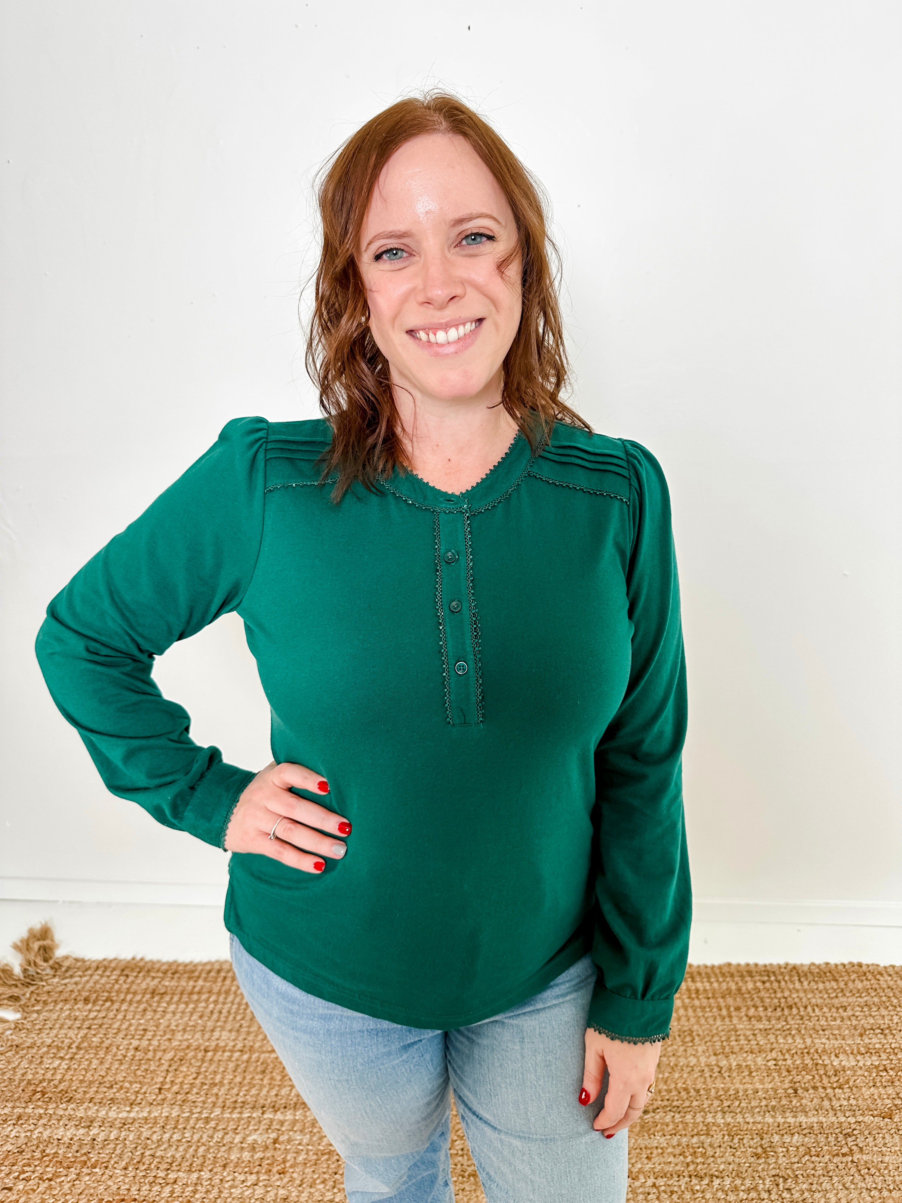 Women's knit blouse with lace detail, made from 100% cotton jersey surplus fabric. Available in Evergreen. Features a collarless band neckline, matching button-front placket, delicate knit lace on shoulders, collar, cuffs, and placket, keyhole buttoned cuffs, and side slits. Medium-weight fabric with light stretch for a straight fit. Available in sizes XS-3X. 