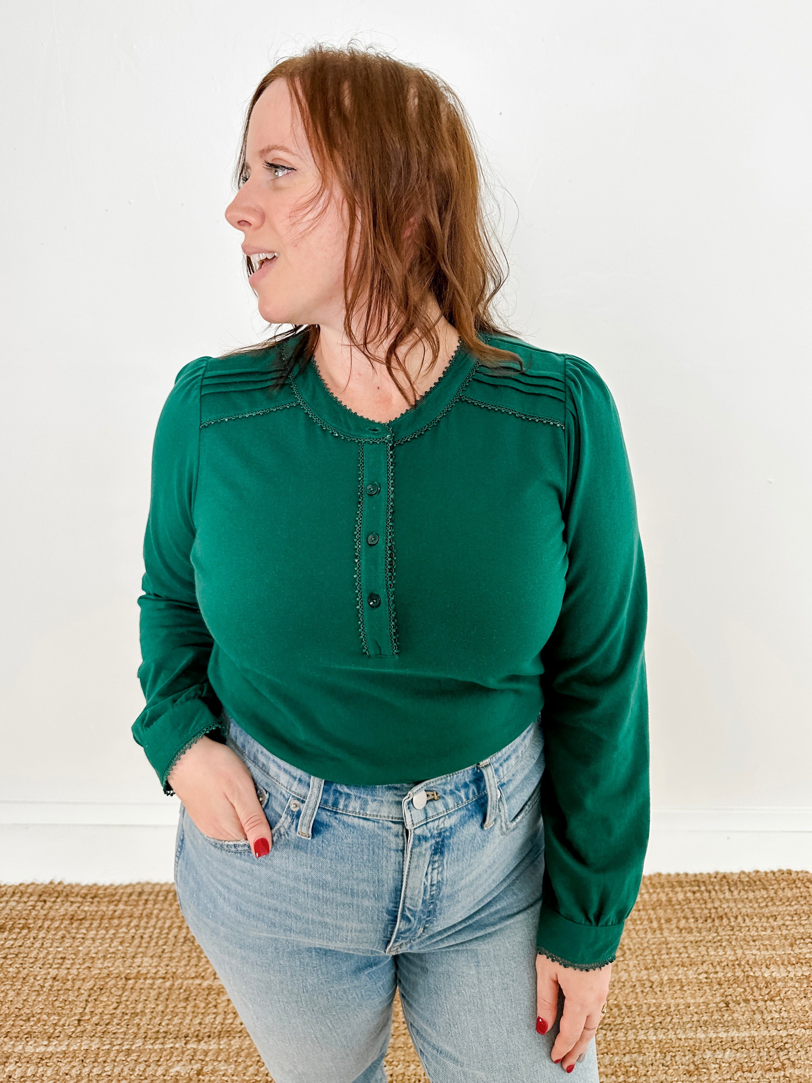 Women's knit blouse with lace detail, made from 100% cotton jersey surplus fabric. Available in Evergreen. Features a collarless band neckline, matching button-front placket, delicate knit lace on shoulders, collar, cuffs, and placket, keyhole buttoned cuffs, and side slits. Medium-weight fabric with light stretch for a straight fit. Available in sizes XS-3X. 