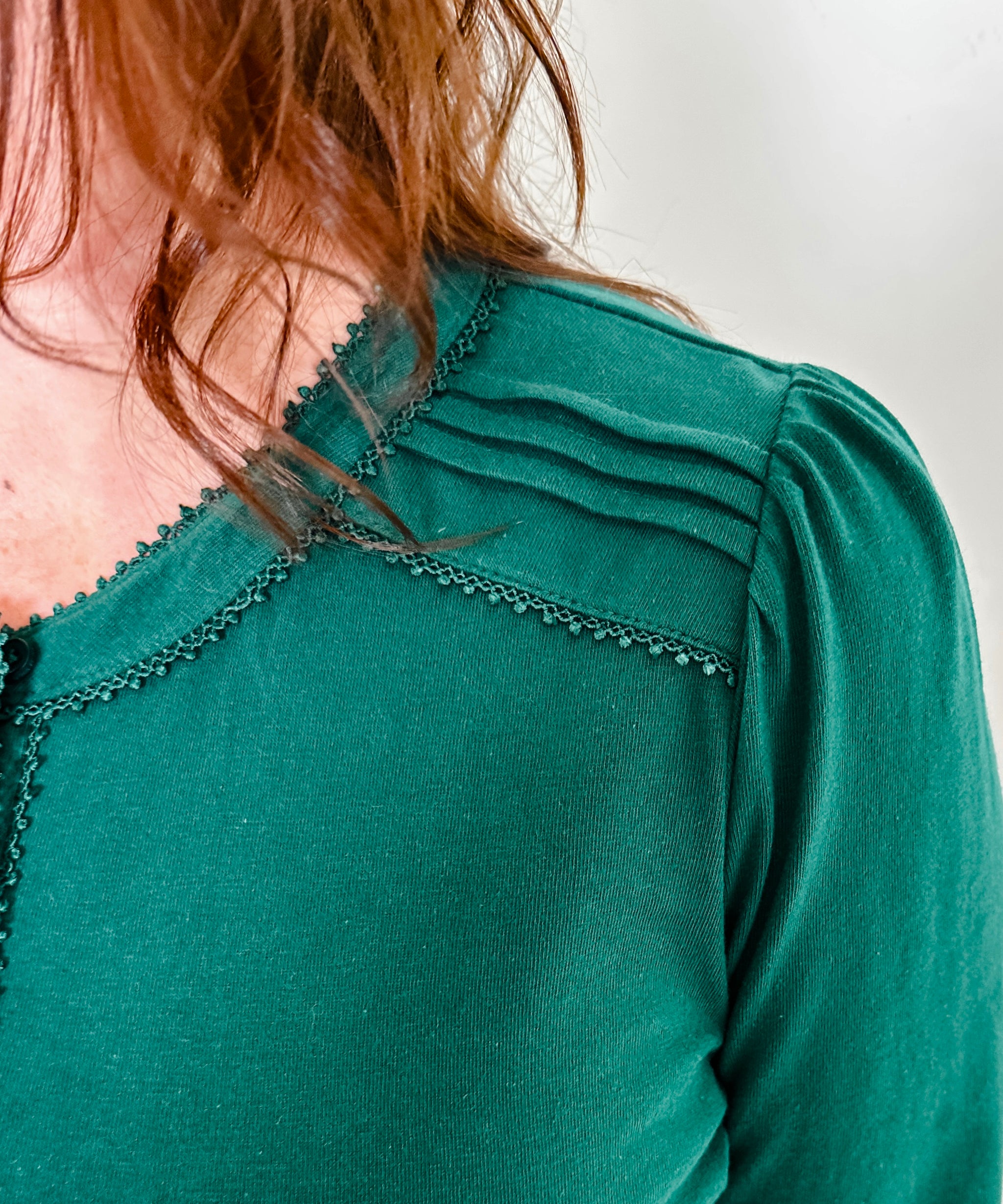 Women's knit blouse with lace detail, made from 100% cotton jersey surplus fabric. Available in Evergreen. Features a collarless band neckline, matching button-front placket, delicate knit lace on shoulders, collar, cuffs, and placket, keyhole buttoned cuffs, and side slits. Medium-weight fabric with light stretch for a straight fit. Available in sizes XS-3X. 