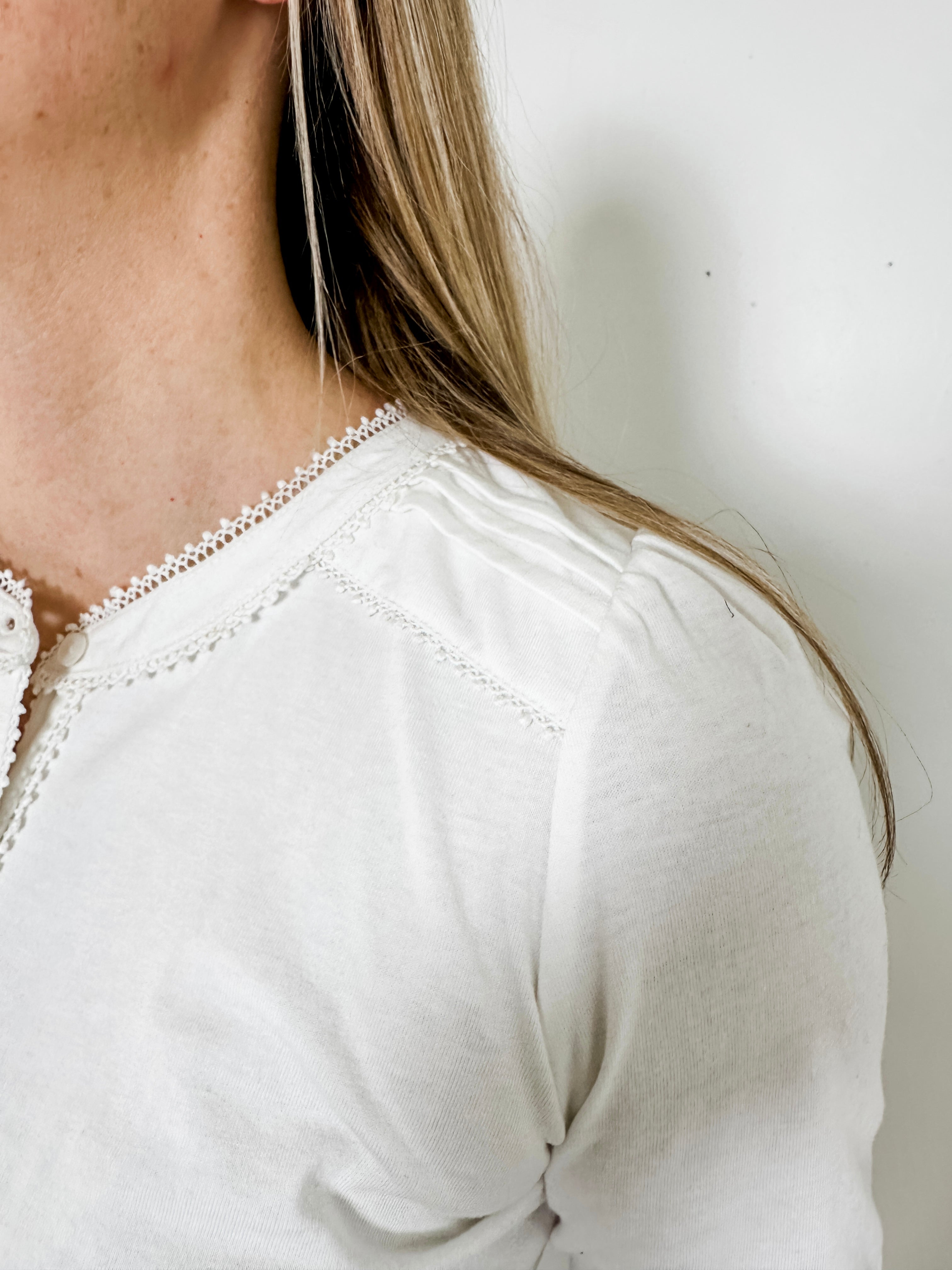 Women's knit blouse with lace detail, made from 100% cotton jersey surplus fabric. Available in white. Features a collarless band neckline, matching button-front placket, delicate knit lace on shoulders, collar, cuffs, and placket, keyhole buttoned cuffs, and side slits. Medium-weight fabric with light stretch for a straight fit. Available in sizes XS-3X. 