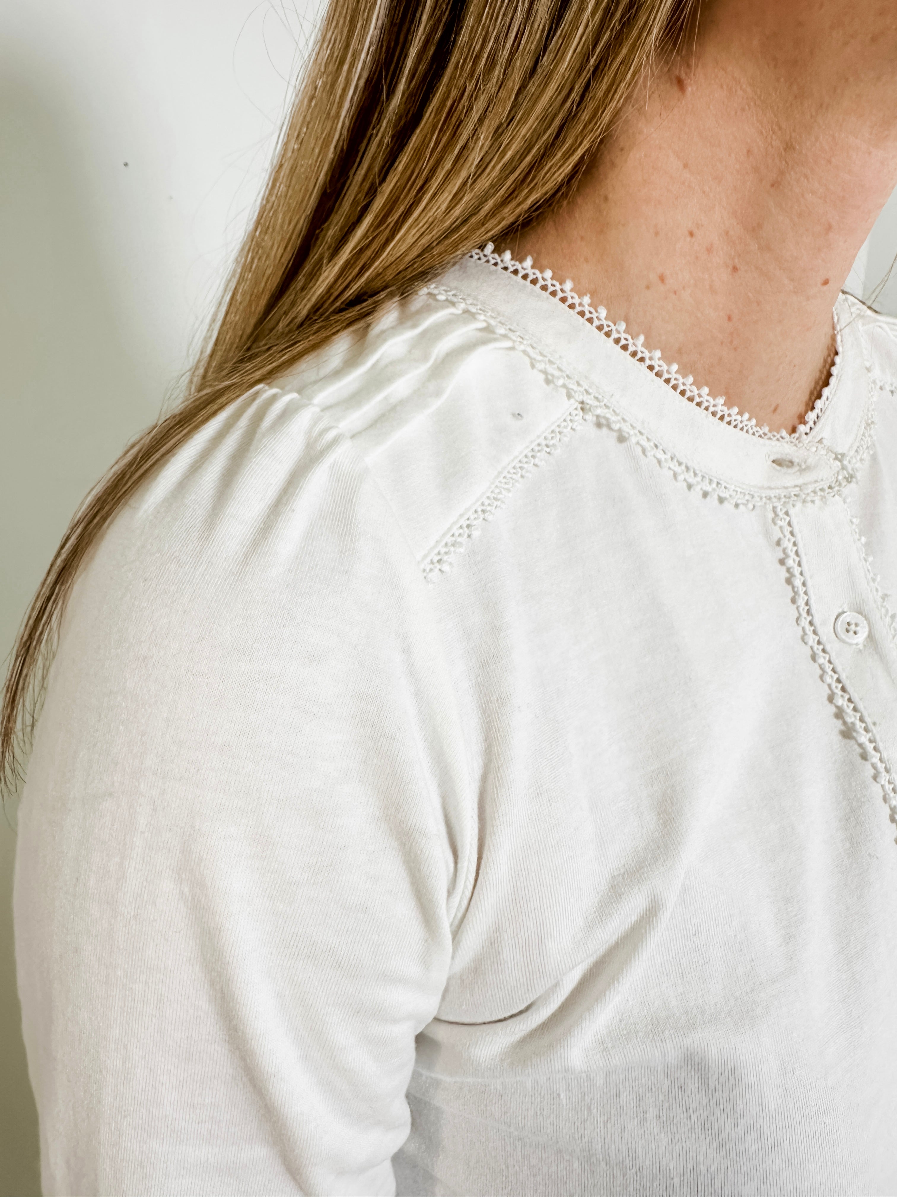 Women's knit blouse with lace detail, made from 100% cotton jersey surplus fabric. Available in white. Features a collarless band neckline, matching button-front placket, delicate knit lace on shoulders, collar, cuffs, and placket, keyhole buttoned cuffs, and side slits. Medium-weight fabric with light stretch for a straight fit. Available in sizes XS-3X. 