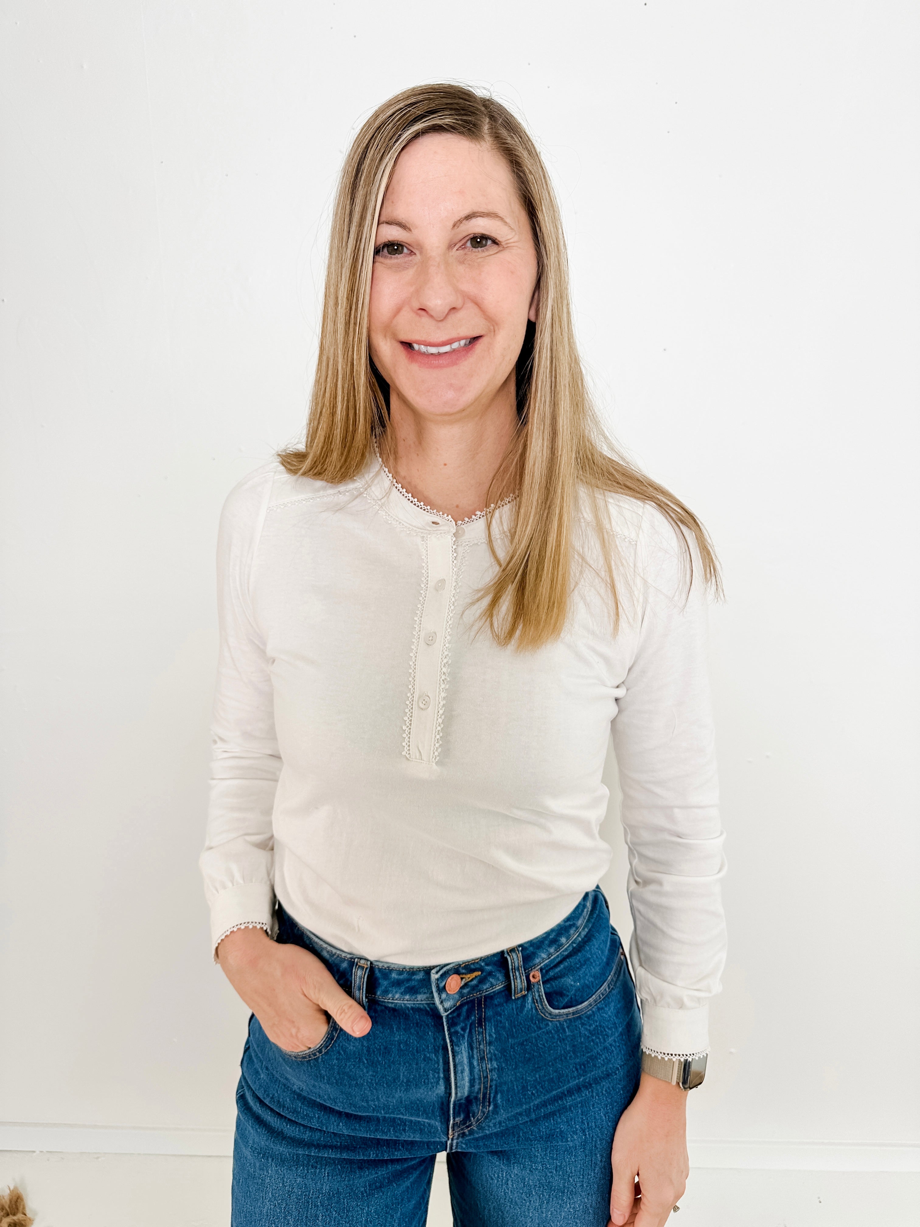 Women's knit blouse with lace detail, made from 100% cotton jersey surplus fabric. Available in white. Features a collarless band neckline, matching button-front placket, delicate knit lace on shoulders, collar, cuffs, and placket, keyhole buttoned cuffs, and side slits. Medium-weight fabric with light stretch for a straight fit. Available in sizes XS-3X. 