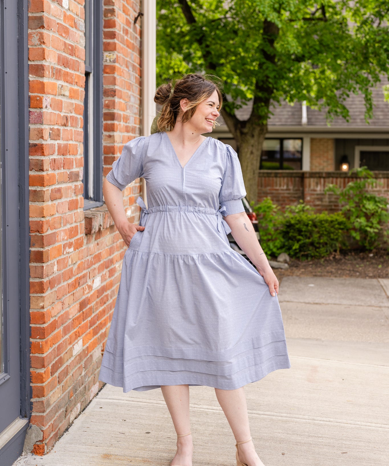 Elegant midi-length dress in surplus 100% cotton with puff sleeves and a unique V-neckline. Features ruching along the bodice, shoulders, and skirt, plus drawstring bows at the waist for a flattering fit. Designed with hidden side pockets, elbow-length keyhole cuff sleeves, and a box-pleated hem. Finished with French seams and a hidden decorative placket.