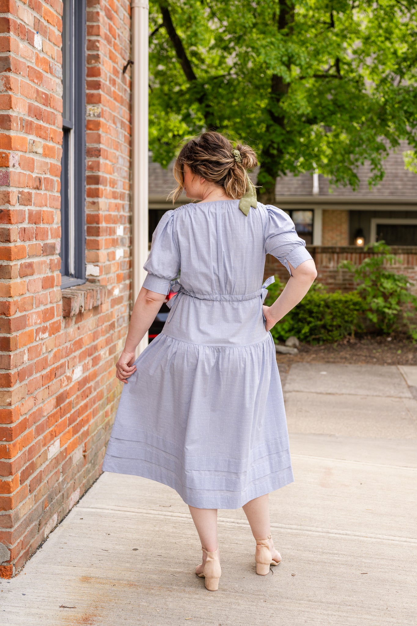 Elegant midi-length dress in surplus 100% cotton with puff sleeves and a unique V-neckline. Features ruching along the bodice, shoulders, and skirt, plus drawstring bows at the waist for a flattering fit. Designed with hidden side pockets, elbow-length keyhole cuff sleeves, and a box-pleated hem. Finished with French seams and a hidden decorative placket.