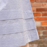 Elegant midi-length dress in surplus 100% cotton with puff sleeves and a unique V-neckline. Features ruching along the bodice, shoulders, and skirt, plus drawstring bows at the waist for a flattering fit. Designed with hidden side pockets, elbow-length keyhole cuff sleeves, and a box-pleated hem. Finished with French seams and a hidden decorative placket.