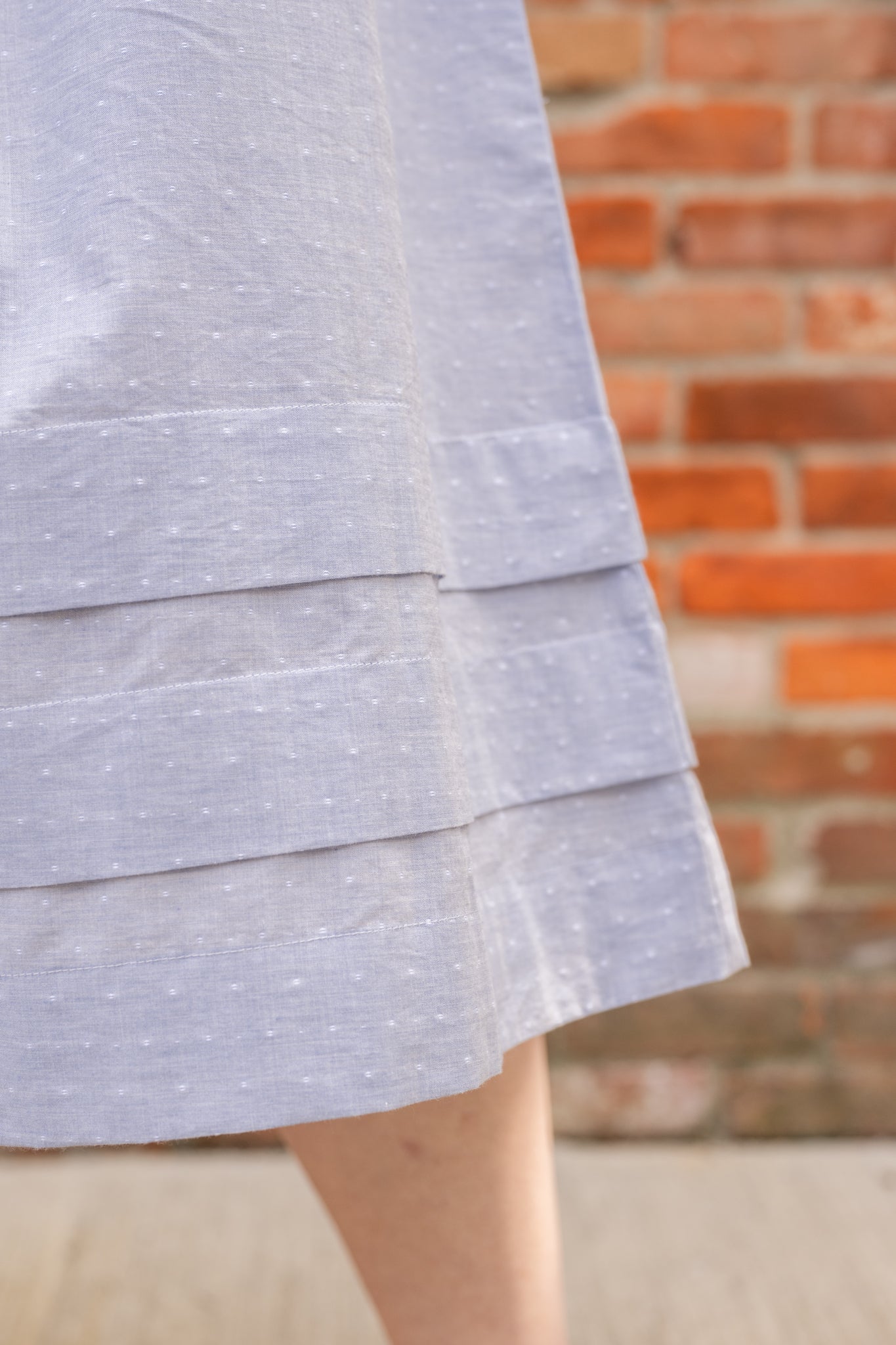 Elegant midi-length dress in surplus 100% cotton with puff sleeves and a unique V-neckline. Features ruching along the bodice, shoulders, and skirt, plus drawstring bows at the waist for a flattering fit. Designed with hidden side pockets, elbow-length keyhole cuff sleeves, and a box-pleated hem. Finished with French seams and a hidden decorative placket.