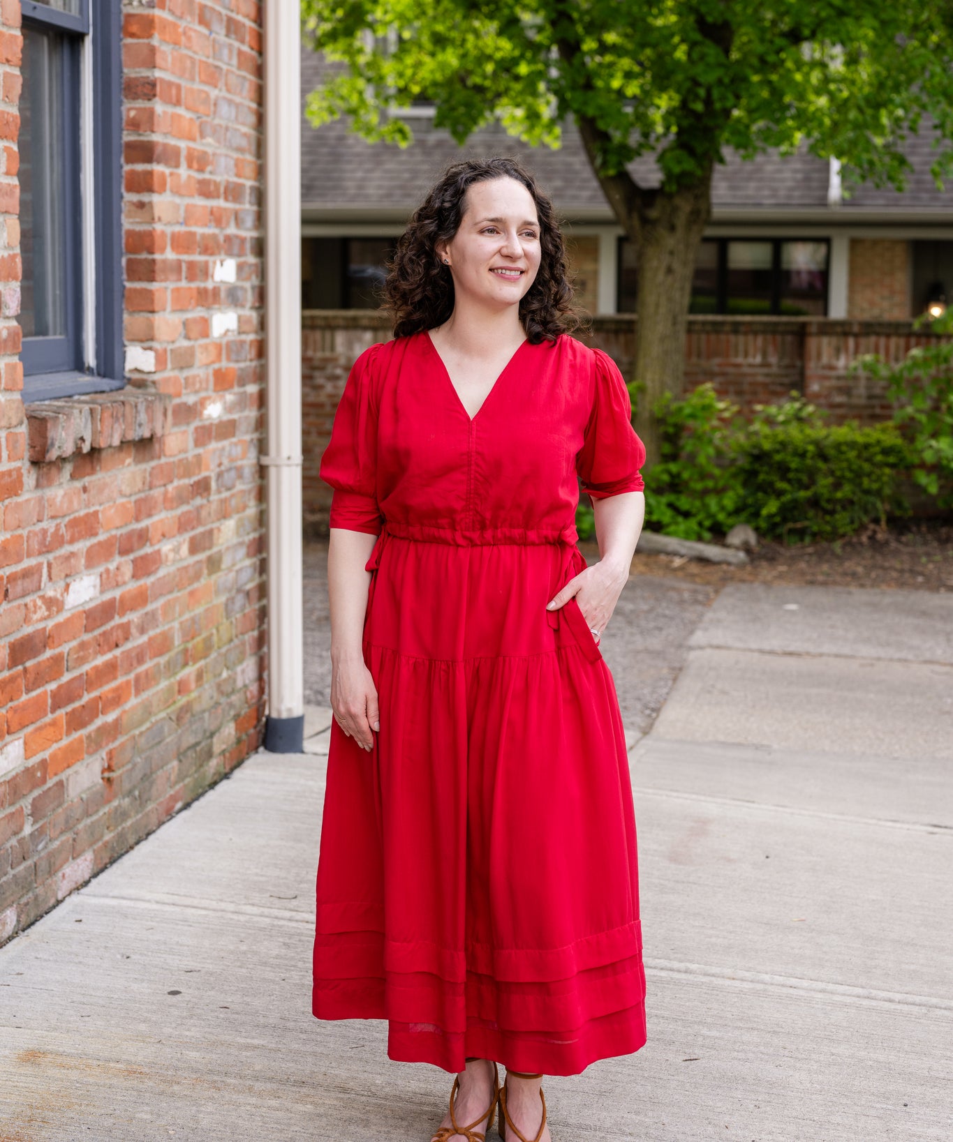 Elegant midi-length dress in surplus 100% cotton with puff sleeves and a unique V-neckline. Features ruching along the bodice, shoulders, and skirt, plus drawstring bows at the waist for a flattering fit. Designed with hidden side pockets, elbow-length keyhole cuff sleeves, and a box-pleated hem. Finished with French seams and a hidden decorative placket.