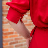 Elegant midi-length dress in surplus 100% cotton with puff sleeves and a unique V-neckline. Features ruching along the bodice, shoulders, and skirt, plus drawstring bows at the waist for a flattering fit. Designed with hidden side pockets, elbow-length keyhole cuff sleeves, and a box-pleated hem. Finished with French seams and a hidden decorative placket.