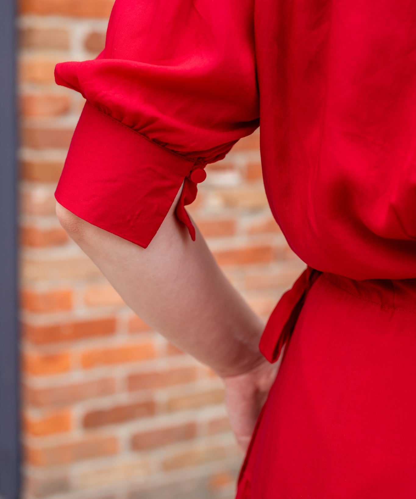 Elegant midi-length dress in surplus 100% cotton with puff sleeves and a unique V-neckline. Features ruching along the bodice, shoulders, and skirt, plus drawstring bows at the waist for a flattering fit. Designed with hidden side pockets, elbow-length keyhole cuff sleeves, and a box-pleated hem. Finished with French seams and a hidden decorative placket.