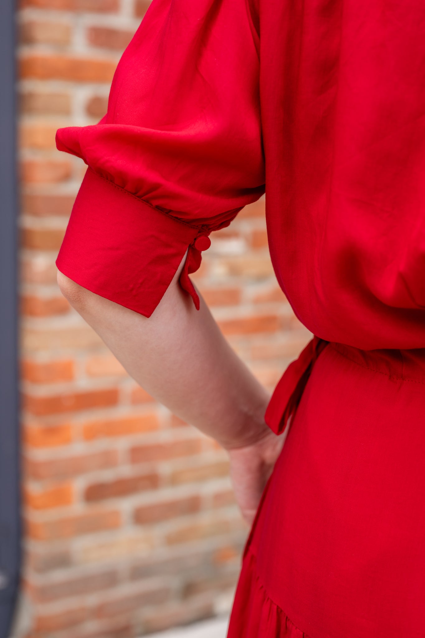 Elegant midi-length dress in surplus 100% cotton with puff sleeves and a unique V-neckline. Features ruching along the bodice, shoulders, and skirt, plus drawstring bows at the waist for a flattering fit. Designed with hidden side pockets, elbow-length keyhole cuff sleeves, and a box-pleated hem. Finished with French seams and a hidden decorative placket.